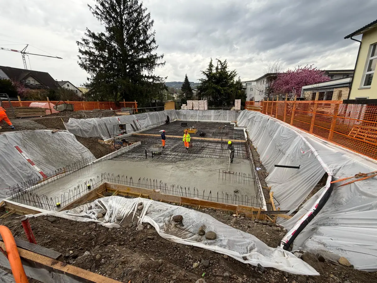 Bauarbeiter verteilen und glätten den frischen Beton auf der Bodenplatte