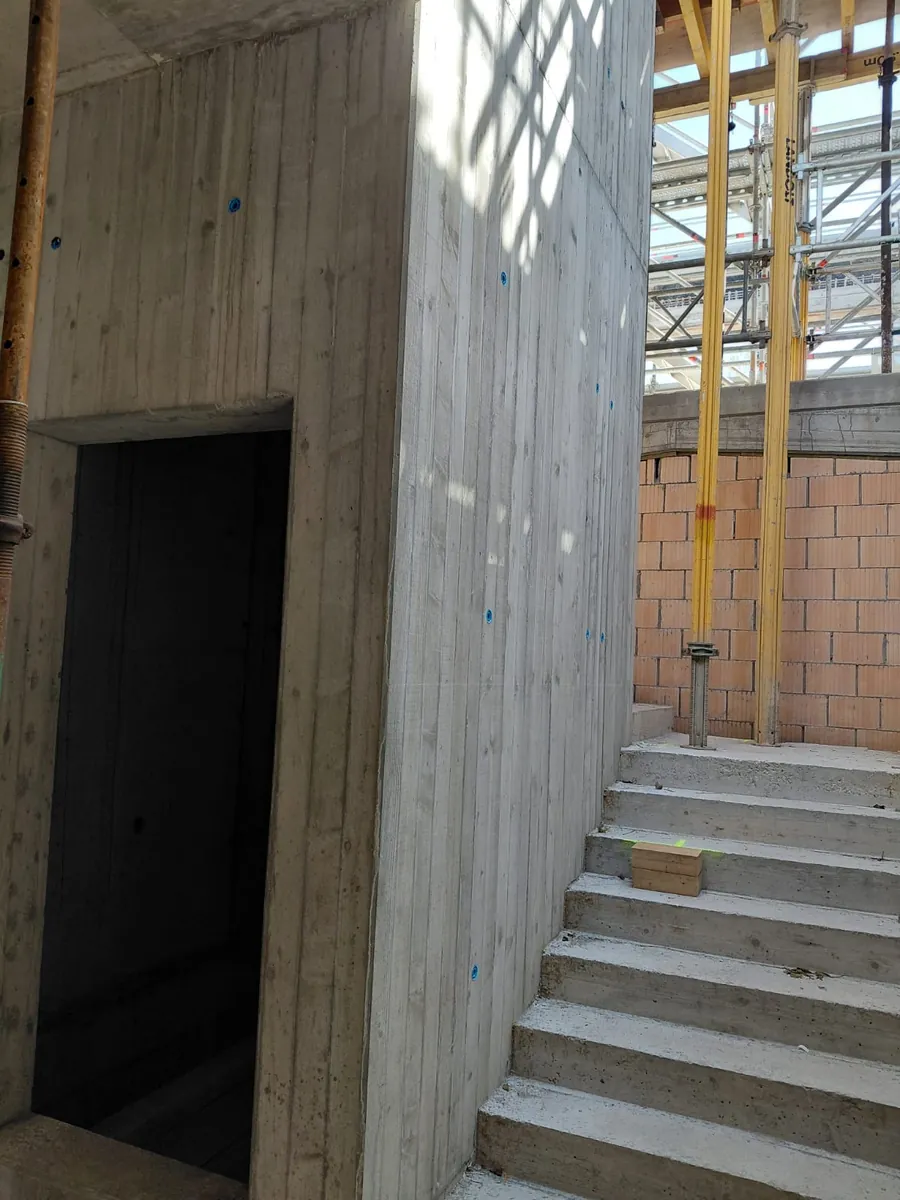 Betonierter Treppenlauf entlang einer Sichtbetonwand in Brettschalung